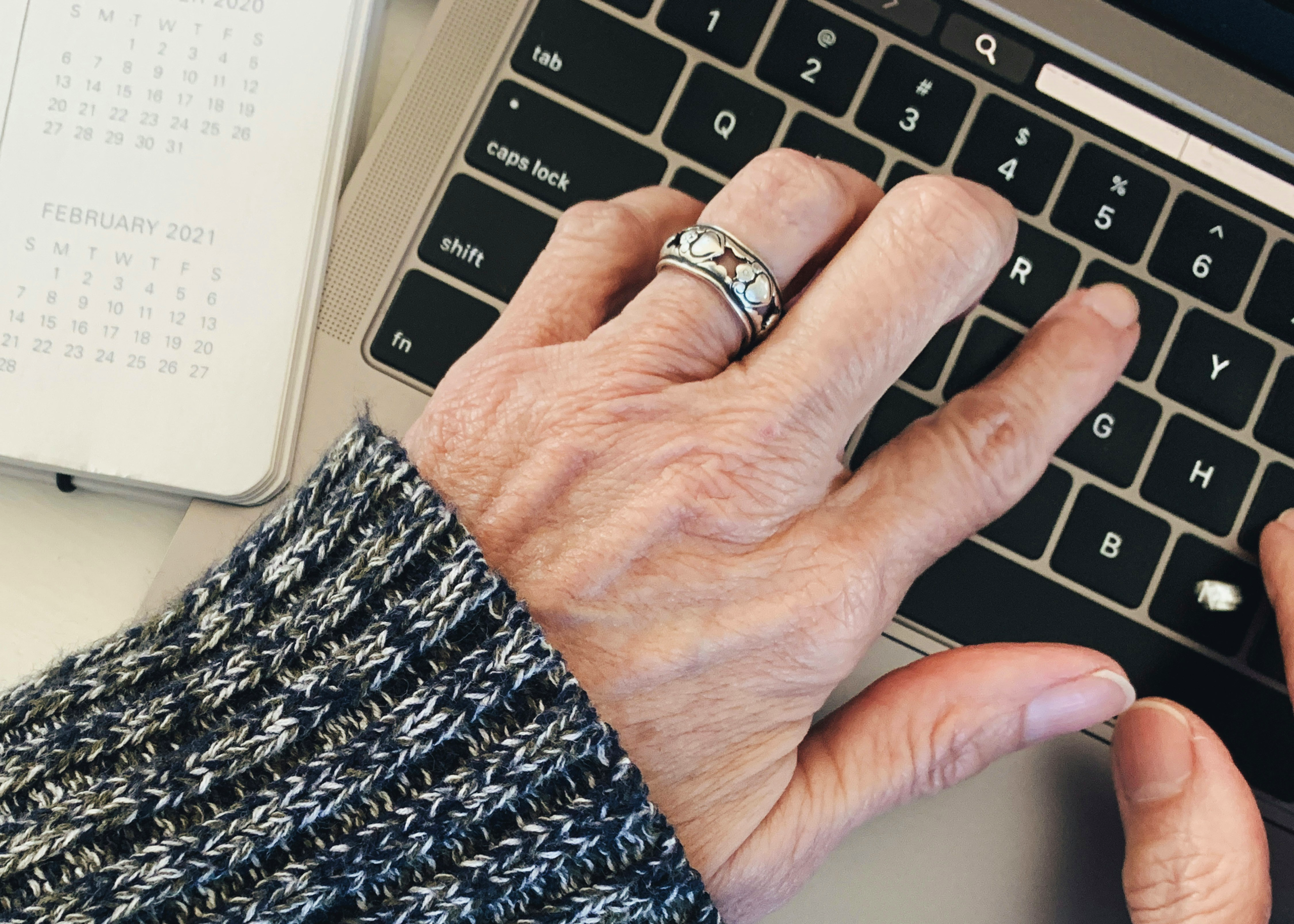 Hand mit silbernem Ring auf Tastatur eines Laptops, daneben ein Kalenderblatt mit dem Monat Februar 2021.